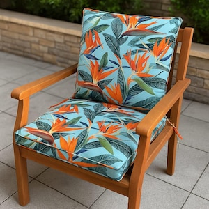 Peut inclure: Chaise de jardin en bois avec un ensemble coussin et oreiller bleu clair. Les coussins présentent un motif floral vibrant de fleurs d'oiseaux de paradis orange et de feuilles vertes. La chaise a une finition en bois naturel.