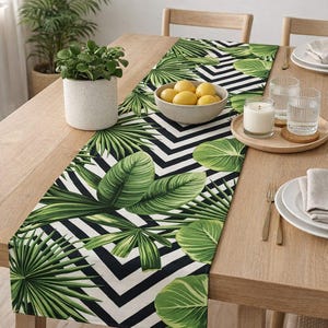 Puede incluir: Una mesa de comedor de madera con un tema tropical. Un camino de mesa con un estampado de hojas verdes y chevrones en blanco y negro es la pieza central. Un cuenco con limones, una vela y la cubertería también son visibles. También hay una planta en maceta y una palmera.