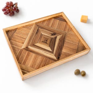 May include: A square wooden serving tray with a geometric design. The tray is made of light and dark brown wood, with a diamond pattern in the center. The tray is empty, ready to be filled with food or other items.