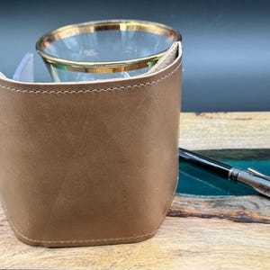 May include: A brown leather wallet with a stitched edge. The wallet is closed and sitting on a wooden surface.