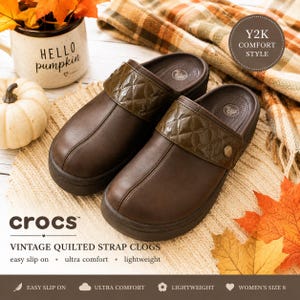 May include: A pair of dark brown clogs featuring a quilted strap across the top. The shoes have a smooth, matte finish on the main body and a glossy, diamond-patterned texture on the strap. Each clog includes a small metallic button detail.