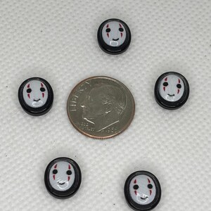 May include: Five small, round, black and white buttons with a smiling face design, arranged around a dime. The buttons have a gray background with red accents for the eyes and mouth. The dime is silver and shows a profile.