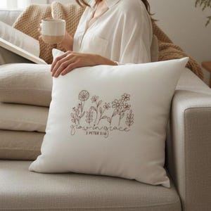 May include: Cream square cushion featuring a floral design and the words "grow in grace" in brown script. The cushion has sketched flowers and leaves. The text "2 Peter 3:18" is below the script.
