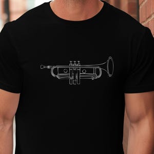 Pode incluir: Camiseta preta com um desenho a traço branco de um trompete. O desenho do trompete está centrado na camiseta, mostrando os detalhes do instrumento. A camiseta é de estilo gola redonda clássica.