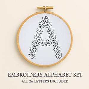 Peut inclure: Un cercle à broder en bois présente un tissu blanc avec un motif floral en forme de "A". La lettre est composée de fleurs noires en forme de marguerite. Le texte "EMBROIDERY ALPHABET SET" et "ALL 26 LETTERS INCLUDED" sont en dessous.