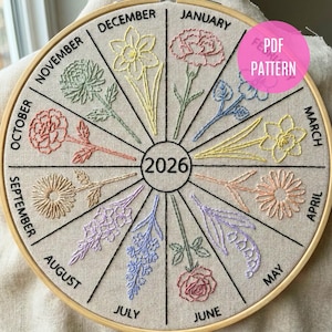 Può includere: Calendario floreale ricamato per il 2026, con sfondo in tessuto beige e telaio in legno. Ogni mese è rappresentato da un fiore diverso, con i nomi dei mesi e l'anno ricamati con filo nero. Un cerchio rosa con "PDF PATTERN" è in alto a destra.