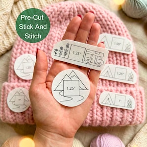 Pode incluir: Um gorro de malha rosa com vários patches pré-cortados para colar e costurar. Os patches apresentam desenhos com tema de acampamento, incluindo uma autocaravana, montanhas e uma fogueira. Os patches medem 2,5 a 3,8 cm.