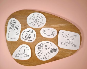 Könnte beinhalten: Eine Sammlung von Aufklebern zum Thema Halloween auf einem Holzbrett. Die Aufkleber zeigen einen Geist, einen Kürbis, einen Hexenhut, Süßigkeiten, ein Spinnennetz und Fledermäuse, alles in schwarzer Linienzeichnung auf weißem Hintergrund.
