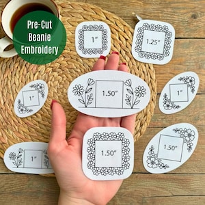 Peut inclure: Plusieurs patchs de broderie pour bonnets pré-découpés blancs, de formes variées, dont des carrés et des ovales. Les patchs présentent des motifs floraux et des découpes carrées avec des mesures de 2,54 cm, 3,18 cm et 3,81 cm pour les projets de broderie. Le texte "Pre-Cut Beanie Embroidery" est dans un cercle vert.