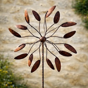 May include: A rustic metal garden wind spinner with a flower-like design. The spinner features a central hub with radiating arms, each holding a series of brown, leaf-shaped elements. The metal has a weathered, rusty appearance, suggesting outdoor use.