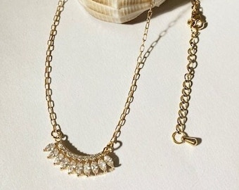 May include: A gold chain necklace with a delicate pendant featuring a row of small, clear, marquise-shaped stones.