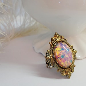 May include: A gold-tone ring with an oval-shaped iridescent opal gemstone set in a detailed filigree frame.