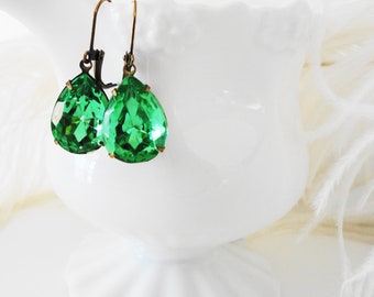 Puede incluir: Un par de pendientes de color verde esmeralda en forma de lágrima con ganchos dorados.