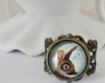 May include: A bronze ring with a round glass cameo featuring a painted image of a rabbit's head. The rabbit has brown fur and white markings around its eyes.