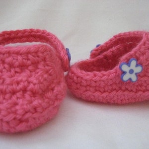 Peut inclure: Une paire de chaussons pour b&eacute;b&eacute; en crochet rose avec des embellissements de fleurs violettes.