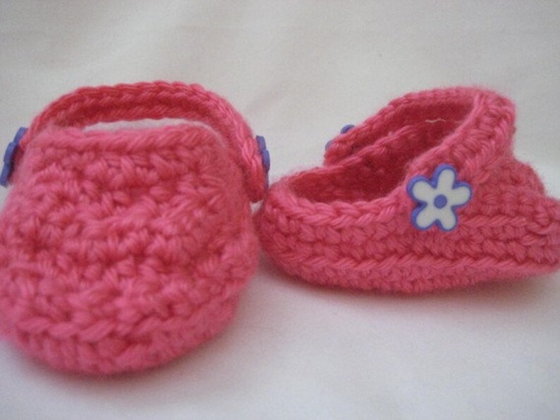 Peut inclure: Une paire de chaussons pour b&eacute;b&eacute; en crochet rose avec des embellissements de fleurs violettes.