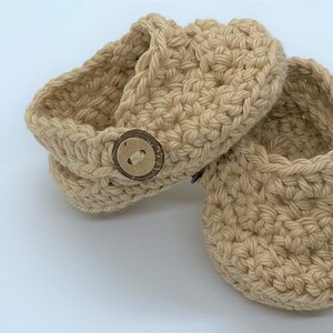 Peut inclure: Une paire de chaussons pour b&eacute;b&eacute; en crochet beige avec des boutons en bois.