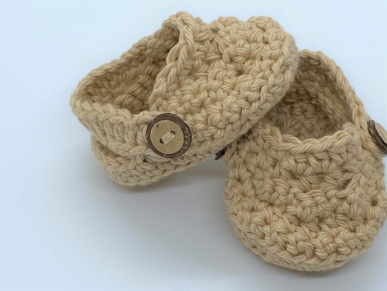 Peut inclure: Une paire de chaussons pour b&eacute;b&eacute; en crochet beige avec des boutons en bois.