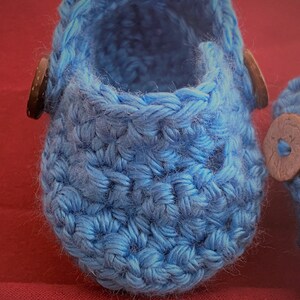 Peut inclure: Une paire de chaussons pour b&eacute;b&eacute; en crochet bleu avec des boutons en bois brun.