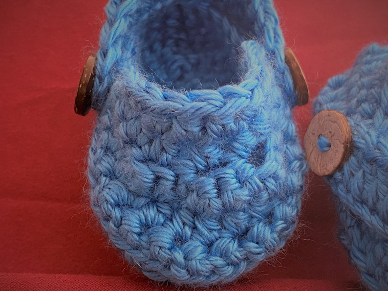 Peut inclure: Une paire de chaussons pour b&eacute;b&eacute; en crochet bleu avec des boutons en bois brun.