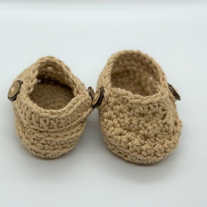Peut inclure: Une paire de chaussons pour b&eacute;b&eacute; en crochet beige avec des boutons en bois.