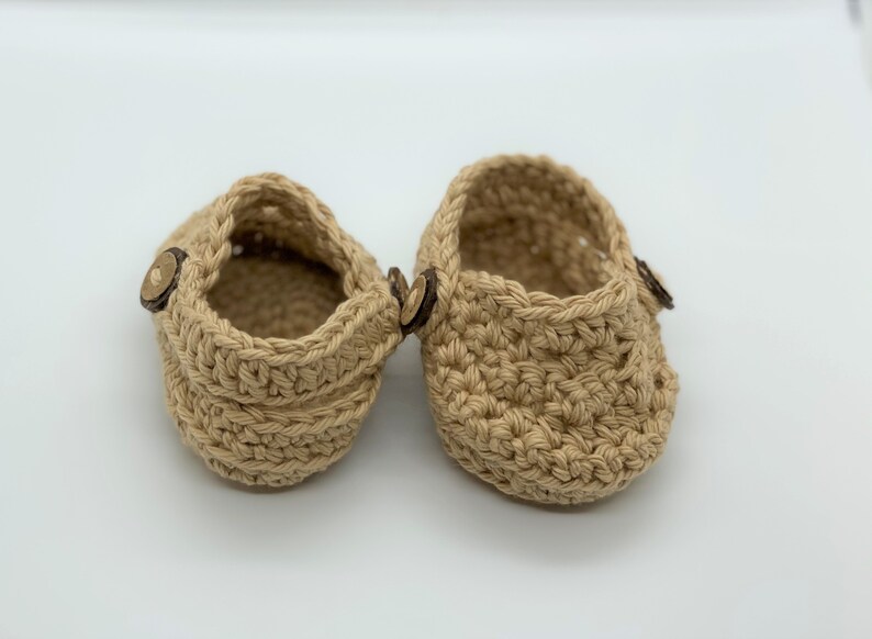 Peut inclure: Une paire de chaussons pour b&eacute;b&eacute; en crochet beige avec des boutons en bois.