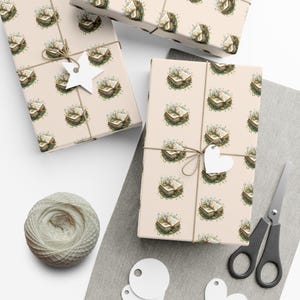 Op de afbeelding: Verschillende ingepakte cadeaus met een herhalend patroon van open boeken omringd door bloemen op een crèmekleurige achtergrond. Elk pakket is vastgebonden met touw en een wit label. Een bol touw, een schaar en labels zijn ook zichtbaar.