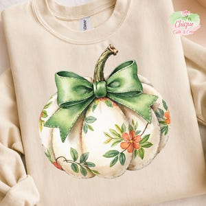Op de afbeelding: Crèmekleurige sweatshirt met een aquarel pompoen ontwerp. De pompoen heeft een groene strik, een groene stengel en is versierd met oranje bloemen en groene bladeren. De woorden "Chique Cute & Cosy" staan in de rechterbovenhoek.