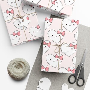 Op de afbeelding: Cadeauverpakte dozen met een roze hartpatroon, vastgebonden met touw en versierd met labels. De harten hebben lachende gezichten en roze strikken. Een bol touw, een schaar en blanco labels zijn ook aanwezig.