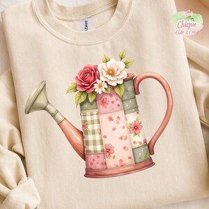 Op de afbeelding: Crèmekleurige sweatshirt met een aquarel illustratie van een roze gieter versierd met bloemen. De gieter heeft een patchwork ontwerp met bloemen- en ruitpatronen. Het ontwerp bevat de tekst "Chique Cute & Cosy".