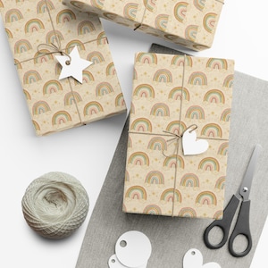 Op de afbeelding: Cadeaudozen verpakt in papier met een herhalend regenboogpatroon in pastelkleuren. De dozen zijn vastgebonden met touw en versierd met stervormige en hartvormige labels. Een bol touw, een schaar en blanco labels zijn ook aanwezig.