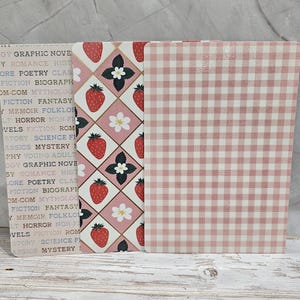 May include: Three decorative paper sheets with different patterns. One has a light pink and white gingham pattern. Another features strawberries, white flowers, and black accents on a pink background. The third has a text-based design with book genres.