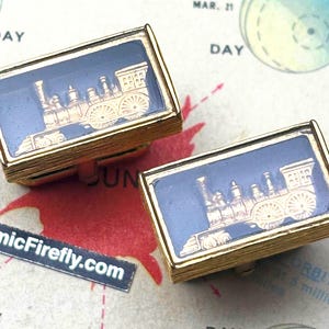 May include: Two gold-toned rectangular cufflinks with a dark blue background. Each cufflink features a gold-colored steam train design. The cufflinks are set against a vintage map background with the text "CosmicFirefly.com".