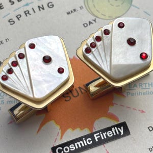 May include: Pair of gold-toned cufflinks with a playing card design. Each cufflink features a white, fan-shaped design with red accents, resembling a hand of cards. The cufflinks are set against a vintage map background.