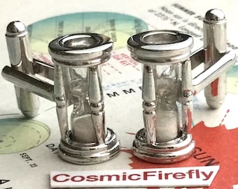 May include: A pair of silver cufflinks with hourglass designs. The hourglasses are filled with a white substance and have a clear glass center.