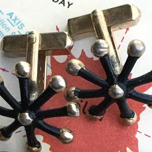 May include: A pair of vintage cufflinks with a distinctive design. Each cufflink has a black, starburst-shaped centrepiece with silver spheres at the arm ends and gold rectangular posts. A stylish accessory.