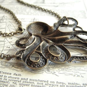 May include: A bronze-colored octopus pendant necklace. The pendant is intricately detailed with a textured surface and open spaces. The necklace chain is also bronze-colored. The background is a vintage nautical map.
