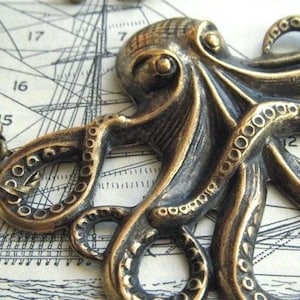 May include: A bronze-toned octopus pendant necklace. The detailed cephalopod design features textured tentacles with suction cups. The necklace is set against a vintage nautical map background, evoking a maritime theme.