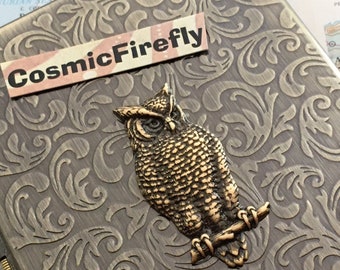 May include: A vintage-style metal box with an ornate design featuring a gold-colored owl perched on a branch. The box has a label that reads "CosmicFirefly".