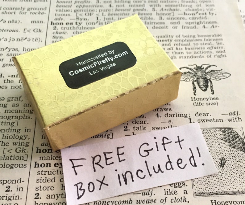 May include: A rectangular, pale yellow gift box with a textured surface and a black label reading Handcrafted by CosmicFirefly.com Las Vegas. A white paper note with the handwritten black text FREE GIFT Box included is placed below.