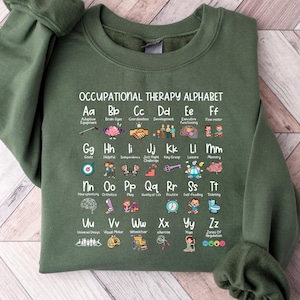 May include: An olive green sweatshirt featuring the "Occupational Therapy Alphabet" in white text. The alphabet is illustrated with colorful images representing various aspects of occupational therapy. The sweatshirt has a crew neck and long sleeves.
