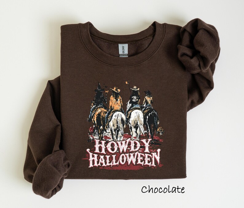 Puede incluir: Sudadera de color chocolate con un gr&aacute;fico de cuatro vaqueros a caballo y el texto "HOWDY HALLOWEEN". La sudadera tiene mangas largas y cuello redondo. La palabra "Chocolate" est&aacute; impresa en la parte inferior.