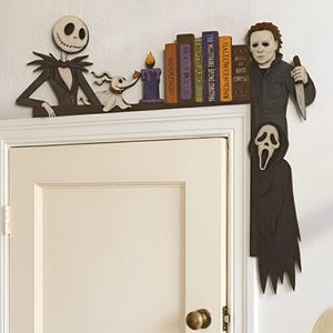 May include: A decorative wooden door corner topper featuring Jack Skellington, Zero, a purple candle, and a row of books titled Hocus Pocus, Beetlejuice, The Nightmare Before Christmas, Halloween, and House of 1000 Corpses, with Michael Myers and Ghostface.