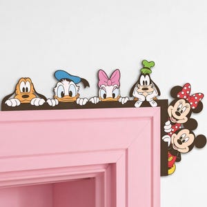 May include: A decorative wooden corner accent featuring colourful cartoon characters including Pluto, Donald Duck, Daisy Duck, Goofy, Minnie Mouse, and Mickey Mouse. The cutout figures are arranged along a dark brown L-shaped frame designed to sit on a door frame.