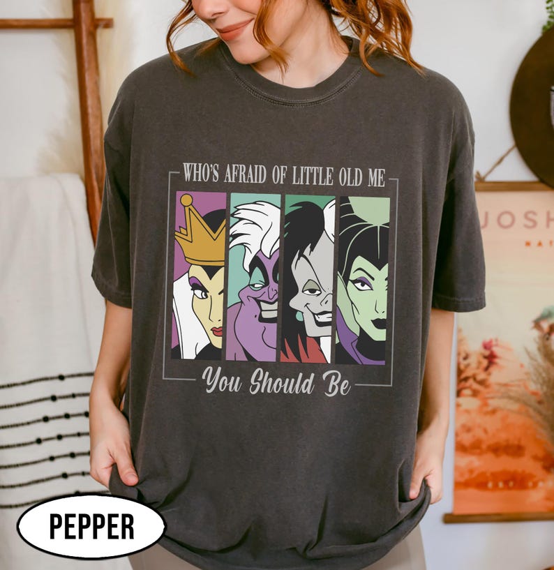 Puede incluir: Camiseta gris oscuro con un gr&aacute;fico de cuatro villanos de dibujos animados en paneles coloridos. El texto de arriba dice "WHO'S AFRAID OF LITTLE OLD ME" y debajo "YOU SHOULD BE". La camiseta tiene un corte holgado y est&aacute; etiquetada como "PEPPER" en la parte inferior.