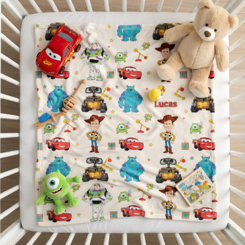 May include: A cream-colored baby blanket featuring cartoon characters from Disney's Toy Story and Monsters, Inc. A red toy car, a green monster plush, and a teddy bear are on the blanket. The name "Lucas" is printed on the blanket.