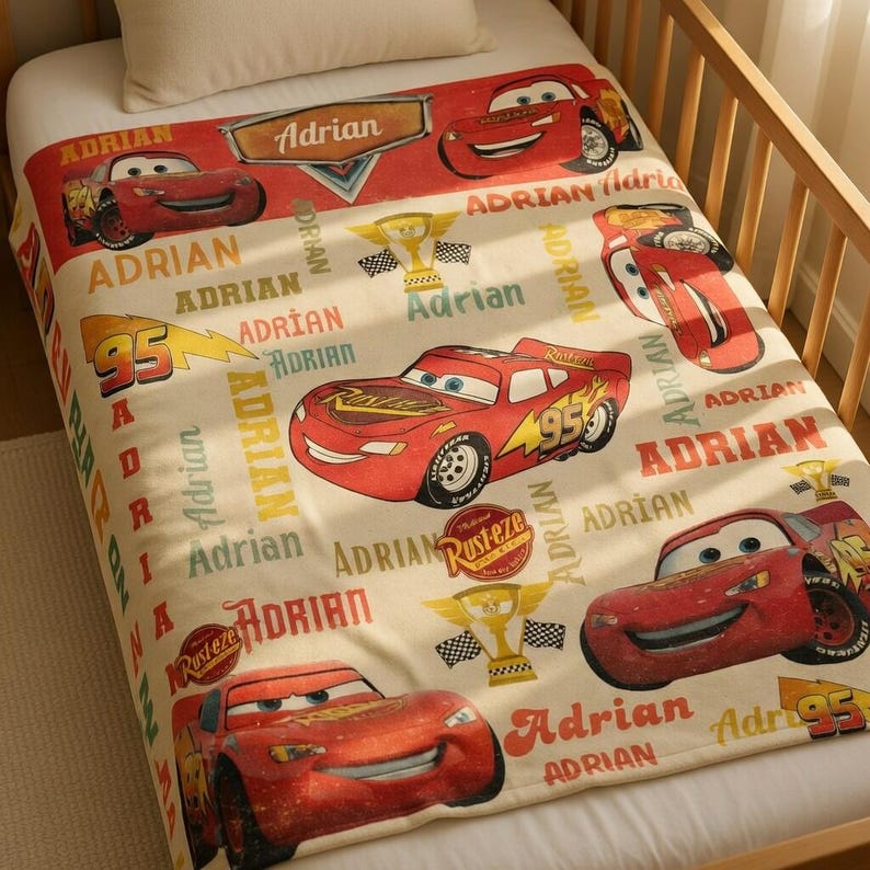 Op de afbeelding: Een cr&egrave;mekleurige deken met het personage Bliksem McQueen uit de film Cars. De deken heeft meerdere afbeeldingen van de rode raceauto, de naam "Adrian" en het nummer "95".
