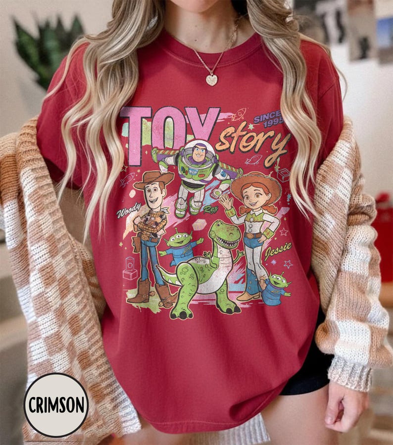May include: Crimson red t-shirt featuring a graphic of Toy Story characters, including Woody, Buzz Lightyear, and Jessie. The words "TOY STORY" and "SINCE 1995" are printed above the characters. The shirt is a crew neck.