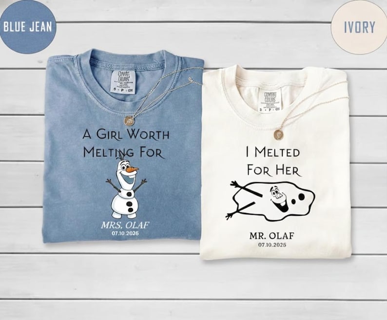 以下が含まれることがあります： 青とアイボリーの2枚の折り畳まれたTシャツ。青いシャツには「A GIRL WORTH MELTING FOR」の文字とオラフのグラフィックが描かれています。アイボリーのシャツには「I MELTED FOR HER」の文字と溶けたオラフのグラフィックが描かれています。どちらのシャツにも日付と「MR. OLAF」または「MRS. OLAF」と書かれています。