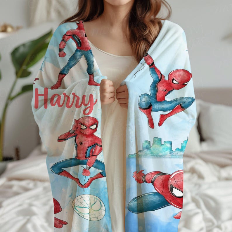 K&ouml;nnte beinhalten: Hellblaue Decke mit Illustrationen von Spider-Man in verschiedenen Actionposen. Der Name "Harry" ist in roter Schrift gedruckt. Die Decke hat einen Aquarellstil.